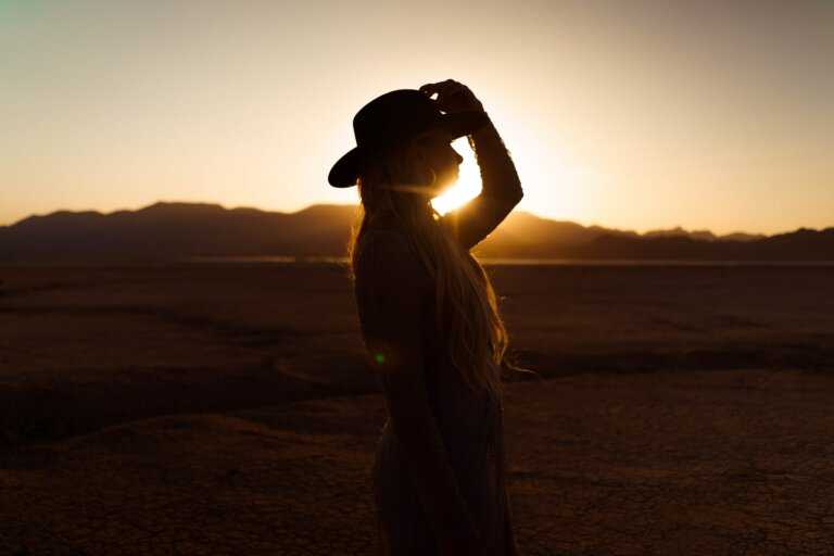 woman in white shirt and black hat standing on beach during sunset