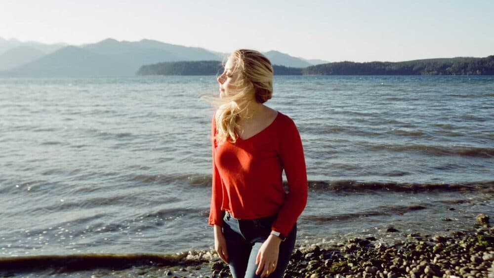 woman in red long sleeve shirt standing on rocky shore during daytime