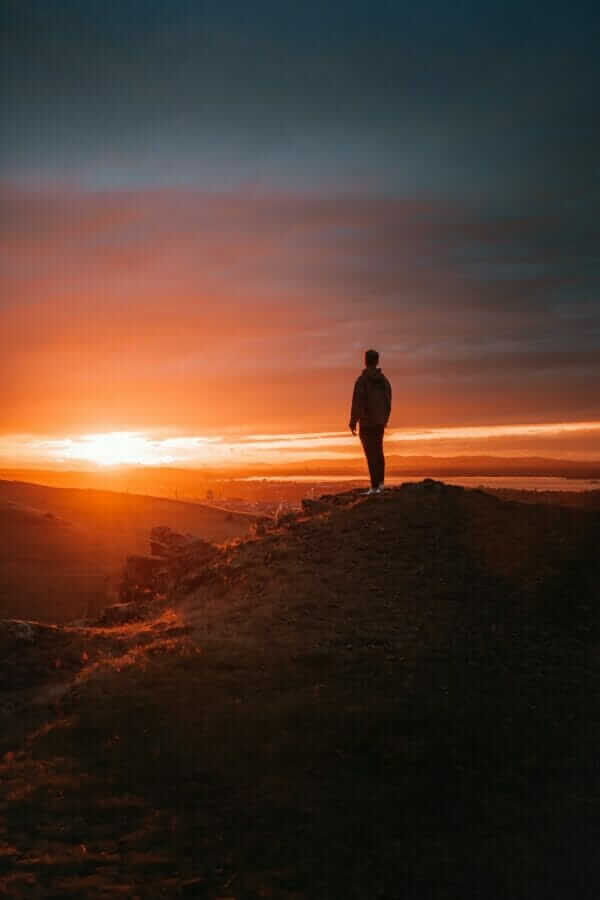 man in black jacket standing on brown rock during sunset