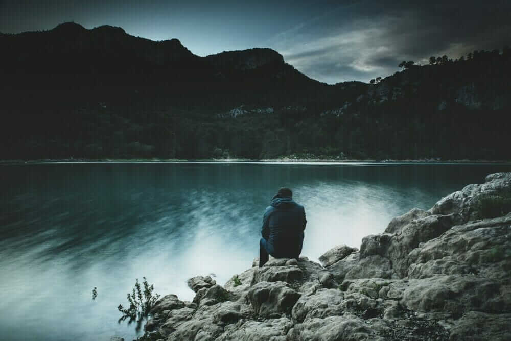 a man sits on a rock staring across a lake at dusk