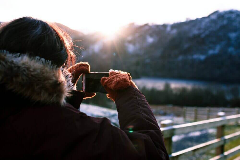person wearing parka holding phone taking photo