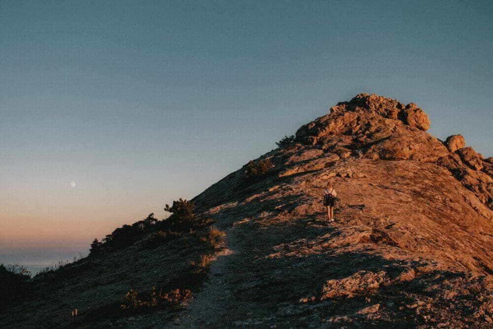 a person hiking up a rocky mountain at sunset