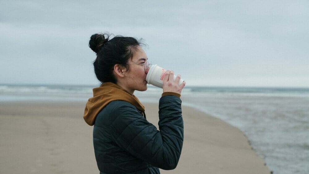a woman drinking from a cup on the beach
