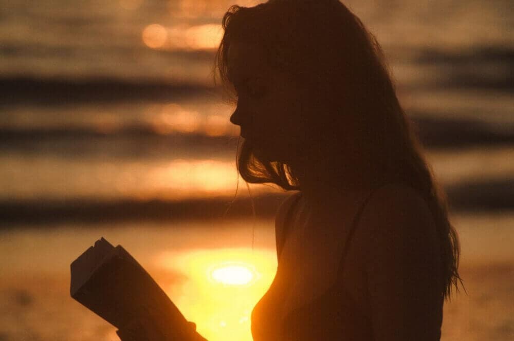 woman reading near body of water during golden hour