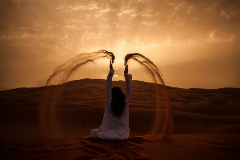 woman sitting on desert while playing sand during golden hour