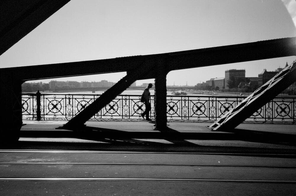 a black and white photo of a person walking across a bridge