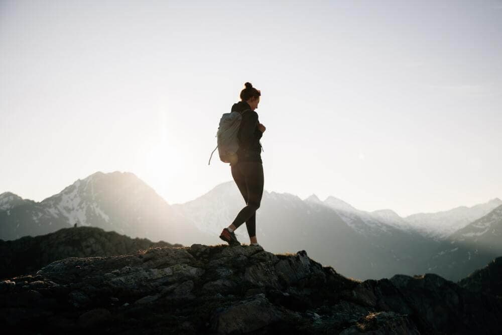 a woman with a backpack standing on top of a mountain