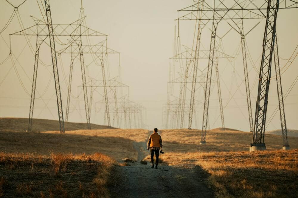 a man walking down a dirt road next to power lines