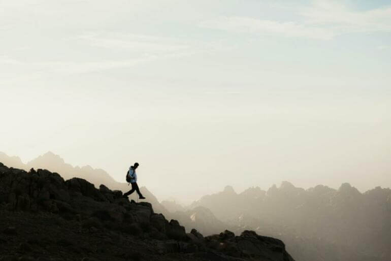 a man running up a mountain with a sky background