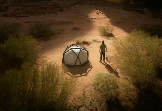 a man standing next to a tent in the desert