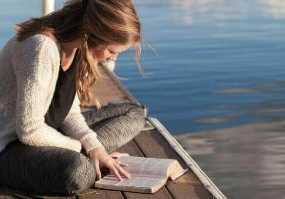 photo of woman reading book near body of water