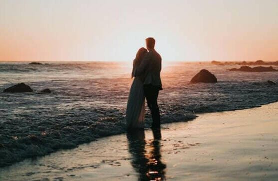 silhouette photo of couple standing on beach watching sunset