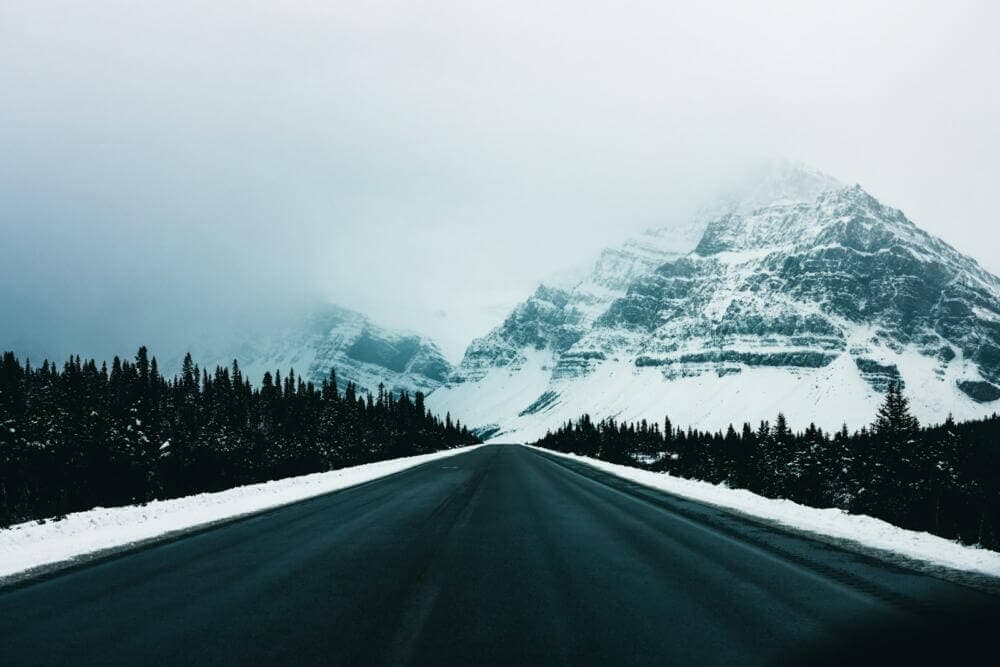a snow covered mountain sits in the distance behind a road