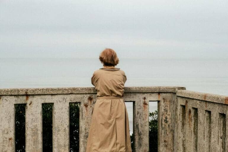 Les Secrets Pour Cultiver Une Confiance En Soi Inébranlable a woman in a trench coat looking out over the ocean