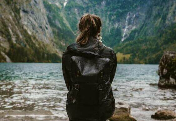 woman in black leather jacket standing on rock near body of water during daytime