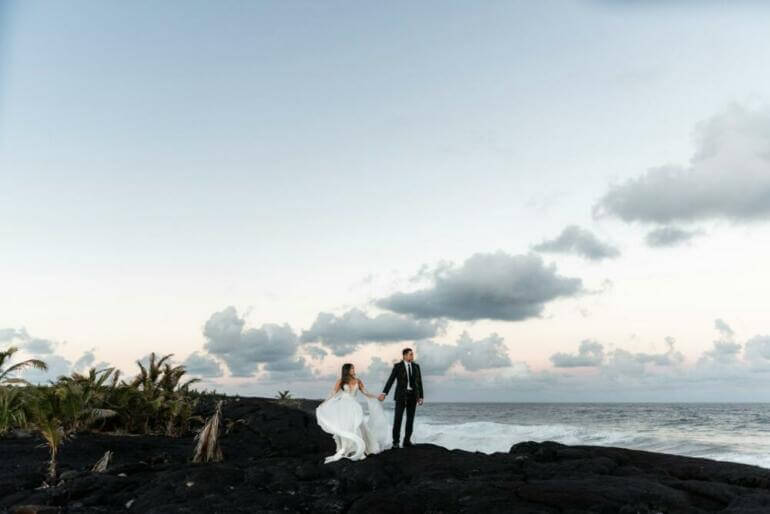 A bride and groom standing on a rocky beach