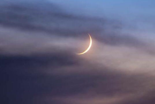 A serene crescent moon above a dramatic sunset silhouetting mountain peaks.