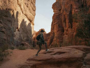 a man in a hat is walking through a canyon